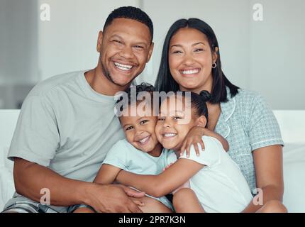 Portrait d'une famille de race mixte jeune heureuse avec deux enfants portant un pyjama et assis à la maison ensemble. Petite sœur aimante et frère s'embrassant tout en passant du temps avec leurs parents le week-end Banque D'Images