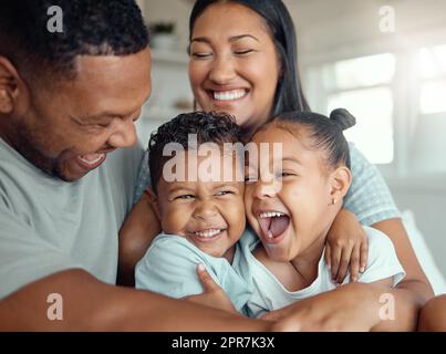 Joyeux drôle de famille de race mixte avec deux enfants portant un pyjama et assis ensemble s'embrassant à la maison. Les parents gais assis avec leur fille et leur fils rient et s'amusent le matin Banque D'Images