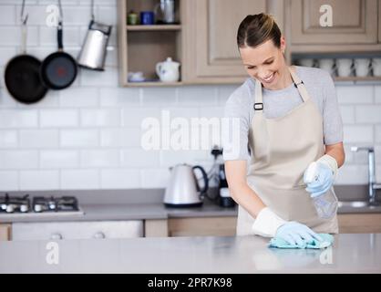 Les surfaces brillantes sont si satisfaisantes. Une jeune femme essuyant une surface de cuisine avec un détergent et un chiffon à la maison. Banque D'Images