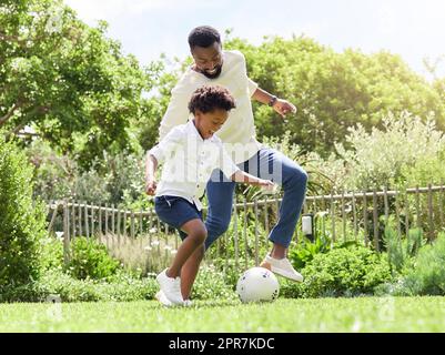 Jouer comme de vraies stars du football. Un père et un fils jouant au football ensemble en plein air. Banque D'Images