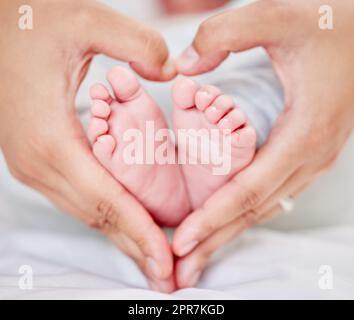 Gros plan des mains d'un parent formant une forme de coeur autour des petits pieds de bébé nouveau-né. Mère aimant son petit bébé. Petit bébé se reposant dans sa chambre de bébé tandis que le parent tient ses pieds. Banque D'Images