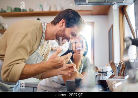 Joyeux jeune couple interracial debout près de la cuisinière tout en cuisinant ensemble dans la cuisine à la maison. Jeune homme caucasien regardant et sentant la nourriture steamy pendant qu'il cuit sur la cuisinière Banque D'Images