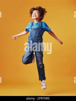 Un enfant de race mixte mignon portant des vêtements décontractés tout en s'amusant et en étant énergique contre un arrière-plan d'imitation orange. Enfant asiatique actif Banque D'Images