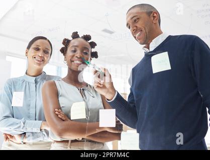 Trois hommes d'affaires heureux écrivant des idées et brainstorming ensemble dans un bureau au travail. Homme d'affaires hispanique faisant une note sur une fenêtre de verre avec des collègues féminins Banque D'Images