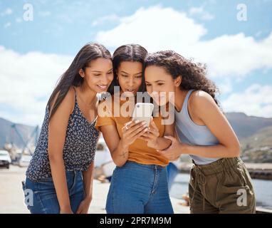 Regardons ensemble. Un groupe de femmes regardant quelque chose sur un téléphone portable ensemble à l'extérieur. Banque D'Images