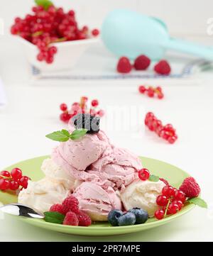 La glace à la vanille et à la framboise se ramasse sur une assiette ronde verte Banque D'Images