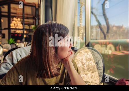 Une belle jeune fille s'assoit dans un restaurant et regarde par la fenêtre Banque D'Images