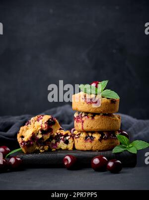 Portion de tarte crumble avec cerises sur un panneau de bois décoré de feuilles de menthe verte, fond noir Banque D'Images