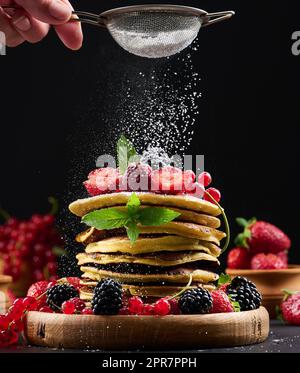 Une pile de crêpes aux fruits frais arrosées de sucre en poudre sur fond noir Banque D'Images