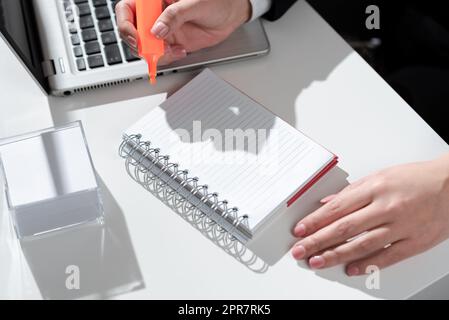 Femme d'affaires écrivant dans un cahier avec marqueur sur le bureau avec notes et Lap Top. Femme en costume tenant le stylo coloré au-dessus du Bloc-notes sur la table avec les Mémos et l'ordinateur. Banque D'Images