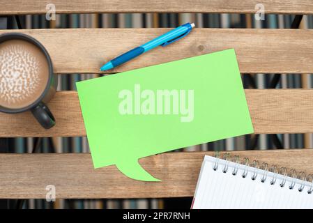 Bulle de parole avec message important sur la table avec café, stylo et cahier ouvert. Ballon de dialogue avec informations de base sur le bureau avec coupe et point de balle. Banque D'Images