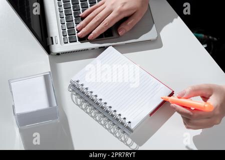 Femme d'affaires écrivant dans un cahier avec marqueur sur le bureau avec notes et Lap Top. Femme en costume tenant le stylo coloré au-dessus du Bloc-notes sur la table avec les Mémos et l'ordinateur. Banque D'Images