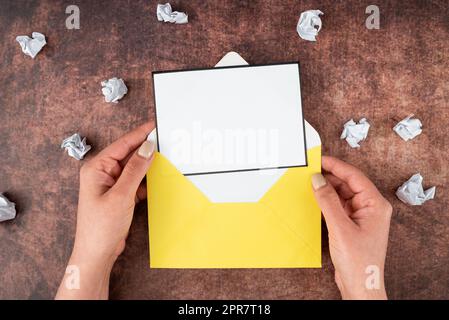 Mains de la femme d'affaires tenant la feuille vierge et l'enveloppe entourée de papier froissé sur le bois. Femme avec une lettre montrant un message crucial. Espace vide pour la publicité. Banque D'Images