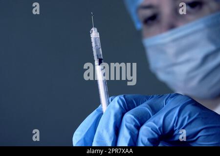 Une femme médecin dans un capuchon médical et un masque tient une seringue médicale dans sa main. Mise au point douce. Banque D'Images