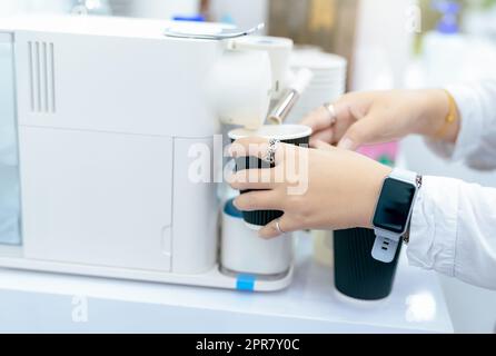 Femme faisant une tasse de café chaud avec machine à café capsule. Femme tenant une tasse noire prenant le café d'une machine à café capsule sur la table. Machine à espresso. Boisson du matin. Équipement moderne. Banque D'Images