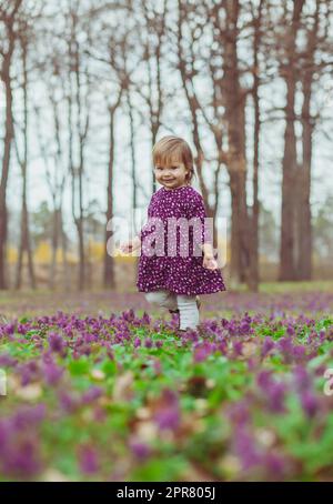 bébé blond dans une robe colorée marche dans une forêt de fleurs Banque D'Images