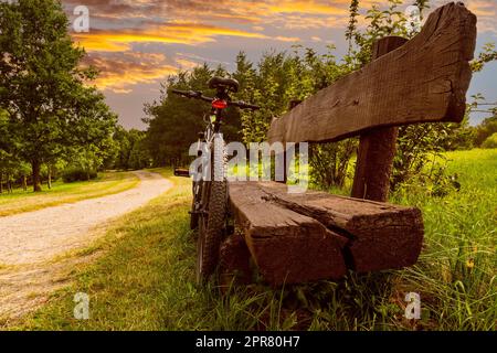Vélo de sport appuyé contre un banc en bois au parc pendant le coucher du soleil Banque D'Images