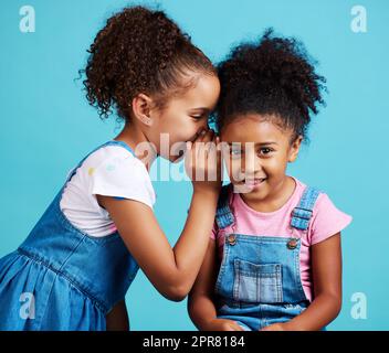 Son notre petit secret. Photo de deux jeunes filles se posant ensemble sur un fond bleu. Banque D'Images