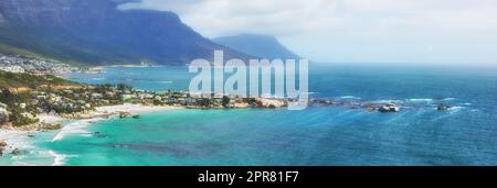 Une vue paisible sur l'océan Clifton au bord de l'Atlantique avec une île et des montagnes en arrière-plan. Une ville entourée d'eau douce bleue et d'un ciel brumeux et nuageux avec espace de copie. Banque D'Images