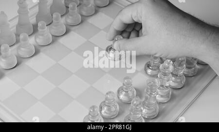 Un échiquier avec une main qui commence à déplacer une pièce d'échecs. Personnages d'échecs en verre clair sur un échiquier Banque D'Images