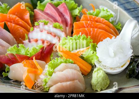 Sashimi mori, ensemble de sashimi mélangé servi dans une assiette en céramique décorée de laitue verte. Buffet de cuisine japonaise. Choix du chef : saumon, hamachi, Ika, Tako, Hotate et hokkigai Banque D'Images