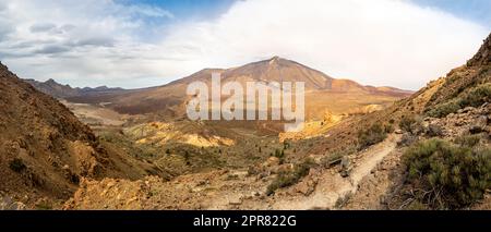 Un sentier de randonnée entouré de paysages volcaniques dans le parc national de Teide offrant une vue panoramique sur la grande vallée et le pic élevé du volcan Teide. Banque D'Images