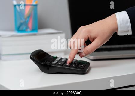 Femme d'affaires appuyant sur la calculatrice avec un doigt sur le bureau avec le haut de tour et les livres. Exécutif pointant sur le bouton du dispositif de calcul sur la table avec ordinateur et crayons. Banque D'Images