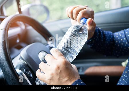 Femme asiatique chauffeur tenant une bouteille pour boire de l'eau tout en conduisant une voiture.Une bouteille d'eau chaude en plastique peut provoquer un incendie. Banque D'Images