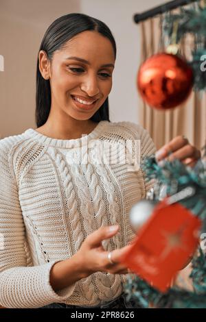 Son début à regarder beaucoup comme Noël. Une jeune femme décorant un arbre de Noël à la maison. Banque D'Images