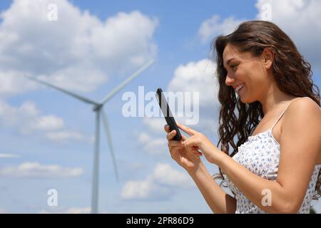 Une femme heureuse utilisant un smartphone dans un parc éolien Banque D'Images