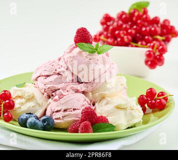 La glace à la vanille et à la framboise se ramasse sur une assiette ronde verte Banque D'Images