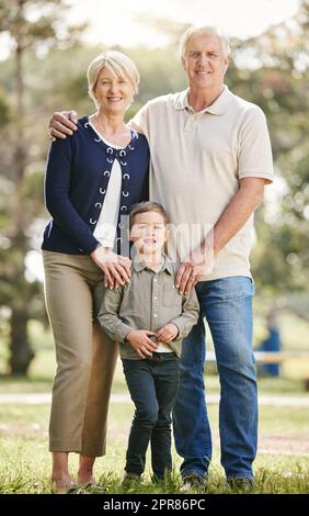 Portrait de grands-parents caucasiens amoureux appréciant du temps avec petit-fils dans la nature. Un petit garçon souriant se liant à la grand-mère et au grand-père. Des aînés heureux et des enfants debout ensemble à l'extérieur Banque D'Images