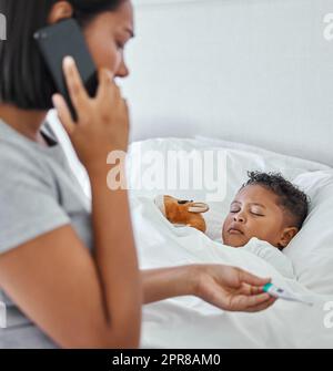 .. Prise de vue d'une femme qui prend la température de ses petits garçons avec un thermomètre au lit à la maison. Banque D'Images