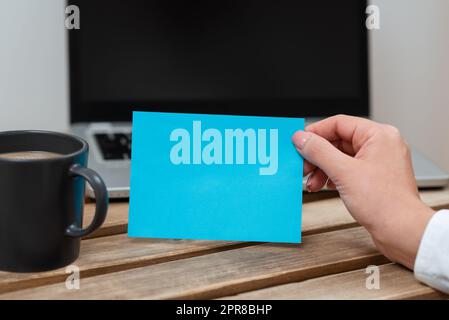 Femme d'affaires tenant une note avec un message important sur la table avec un plateau et un café. Femme présentant des informations sur le papier sur le bureau avec ordinateur et la tasse. Banque D'Images