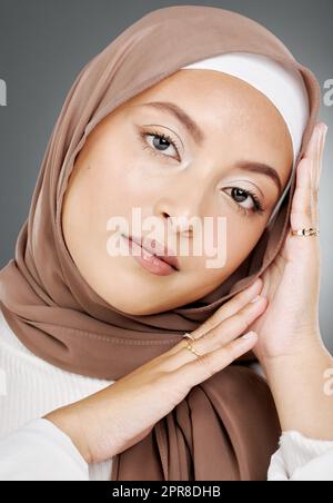 Portrait d'un élégant et lumineux des femmes musulmanes face isolée sur fond gris de studio. Jeune femme portant un hijab ou un foulard, montrant ses extensions de cils, bijoux et routine de peau Banque D'Images