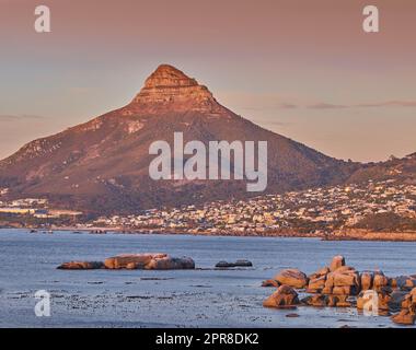 Copiez l'espace avec une vue panoramique sur le paysage d'une ville côtière le long de la montagne de Lions Head au Cap, en Afrique du Sud, sur un fond de ciel crépuscule. Vue panoramique sur la mer avec un point de repère emblématique au coucher du soleil Banque D'Images