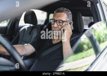 Senior dans sa 70s conduite d'une voiture et à l'aide de son téléphone mobile Banque D'Images