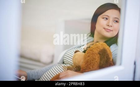 Elle a déjà acheté des babayes pour la première fois. Une jeune femme attrayante se détendant avec un ours en peluche sur le canapé à la maison. Banque D'Images