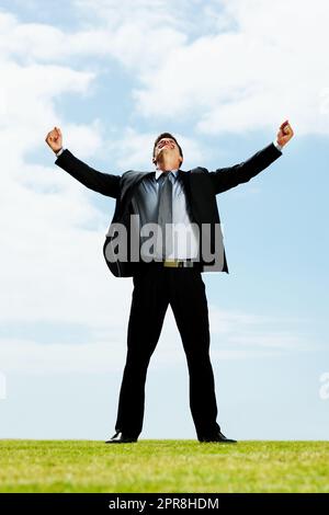 Célébration - bon homme d'affaires avec ses bras étendus sur un terrain. Portrait en longueur d'un homme d'affaires qui réussit à regarder vers le haut avec ses bras étirés sur un champ. Banque D'Images