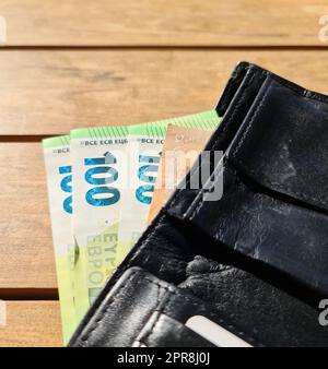 Un portefeuille en cuir noir contenant plusieurs billets de 100 euros . Banque D'Images