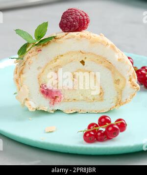 Rouleau de meringue cuit avec baies rouges sur une assiette ronde, fond blanc Banque D'Images