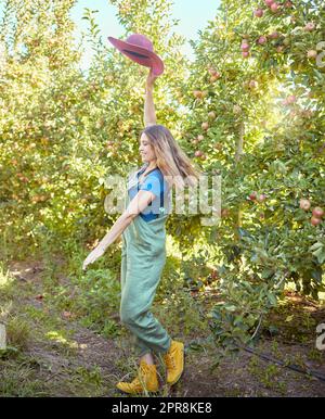 Joyeux fermier se sentant optimiste et accompli pour la saison de récolte de fruits frais biologiques. Une jeune femme heureuse et dynamique qui sautait pour la joie sur une ferme durable de vergers de pommes par beau temps ensoleillé. Banque D'Images