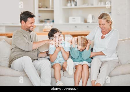 Tickle, tickle. Un adorable petit garçon et une fille qui est tickée par leurs parents sur le canapé à la maison. Banque D'Images