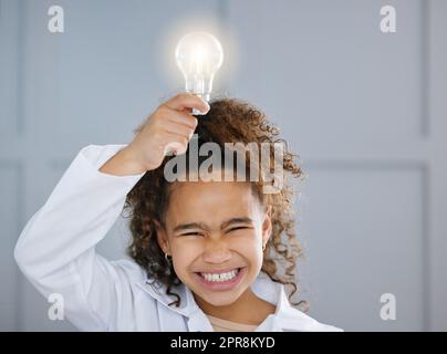 Une adorable petite fille portant un manteau et tenant une ampoule au-dessus de sa tête. Banque D'Images