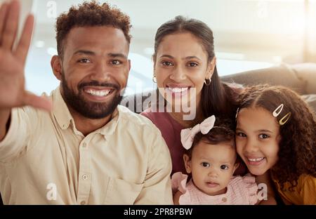 Portrait de parents de race mixte souriants prenant le selfie avec des filles adorables. Une famille hispanique heureuse prend des photos sur les réseaux sociaux à la maison. Mère, père et petites filles se liant tout en prenant la photo Banque D'Images