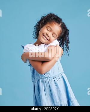 Adorable adorable petite fille adorable et adorable, elle a l'air heureuse tout en s'embrassant. Mignon enfant avec l'estime de soi positive sur fond bleu de studio Banque D'Images