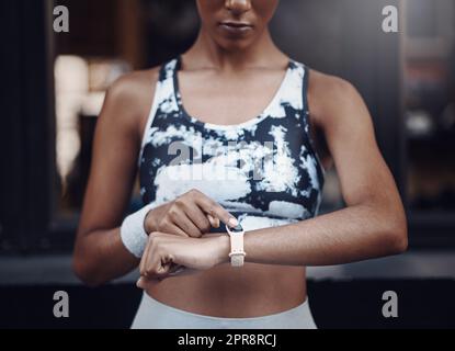 Gros plan d'une femme de course mixte qui vérifie son temps sur une montre numérique avec écran vide lors de la course à l'extérieur. Une athlète féminine portant un tracker d'activité sur le bras pour surveiller les progrès, la fréquence cardiaque et les calories brûlées pendant l'entraînement en ville Banque D'Images