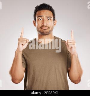 Beau jeune homme de course mixte pointant vers le copyspace tout en se tenant en studio isolé sur un fond gris. Vous n'êtes pas certain de faire de la publicité hispanique ou de soutenir votre produit, votre entreprise ou votre idée Banque D'Images