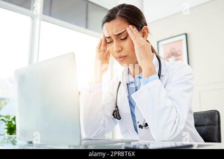 Gros plan d'un jeune médecin de race mixte qui a l'air inquiet et qui souffre d'un mal de tête en travaillant sur un ordinateur dans son bureau. Femme hispanique souffrant de douleurs à la tête et de stress à l'hôpital Banque D'Images