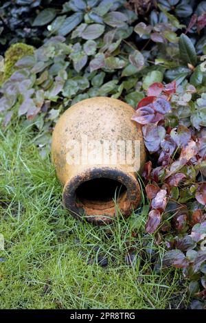 Un pot en céramique simple, ancien, vintage et décoratif allongé sur de l'herbe verte non coupée dans un jardin intérieur à l'extérieur. Décoration extérieure rustique, négligée et laissée au temps dehors dans la cour Banque D'Images